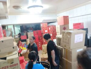 室內大量紙箱與禮品袋散落，兩名工作人員討論商業搬遷分配，成傑搬家執行