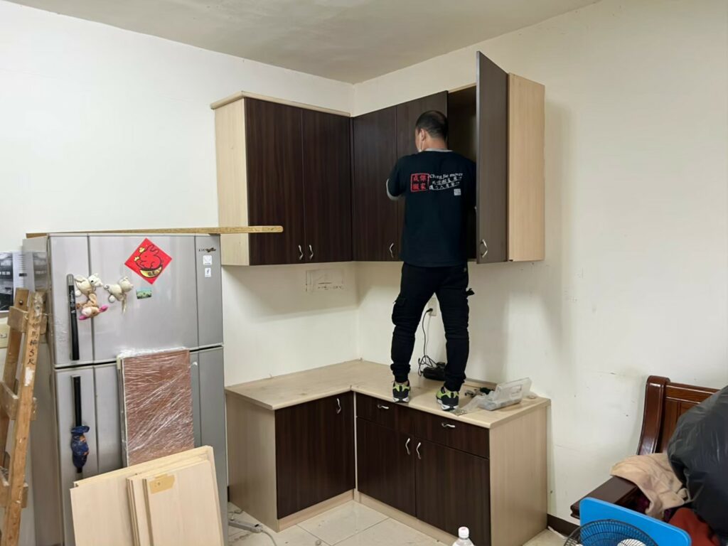 成傑搬家工作人員站在廚房將深木色吊櫃安裝至牆面,代客搬家廚具安裝服務