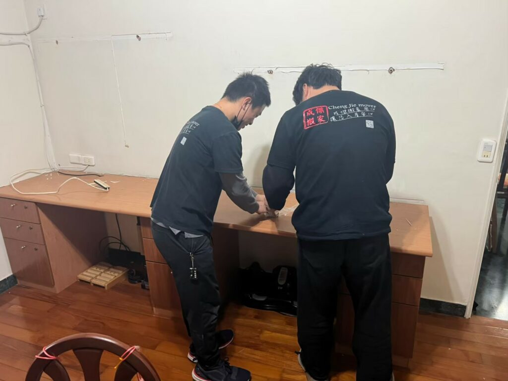 成傑搬家兩名工作人員合力拆解或移動木製長型辦公桌,代客搬家辦公室遷移作業