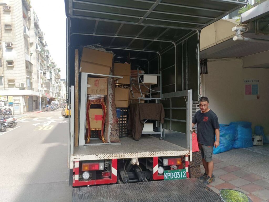師傅站在廂型貨車車斗旁,車內裝載家具箱物及神桌,家庭搬家出發前整備