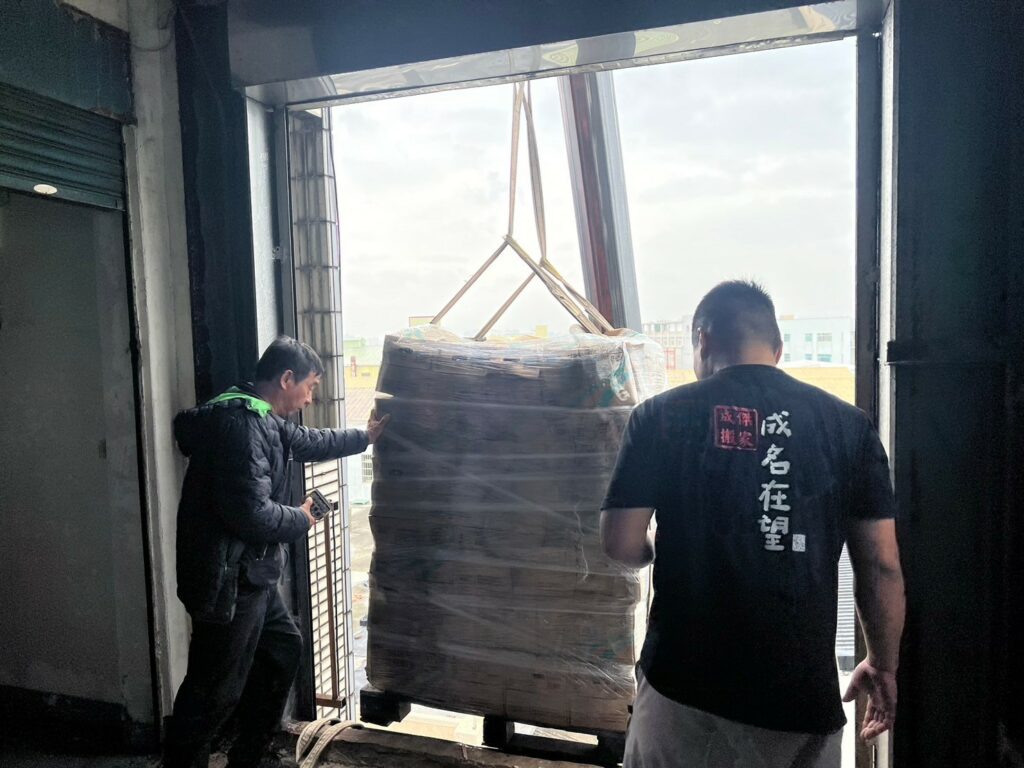 成傑搬家工作人員在倉庫以吊具起吊整托盤紙箱貨物,代客搬家大量物件吊運