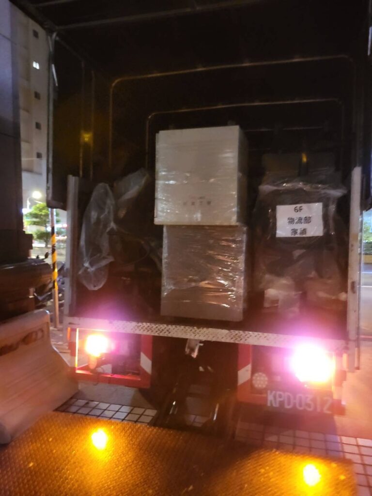 夜間廂型貨車尾板半開，車內可見標有物流標籤的包裝家具，回頭車搬家運送