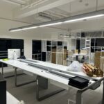 新辦公室內白色長桌與 iMac 電腦擺放整齊,仍有紙箱待歸位,家庭搬家搬入後整理