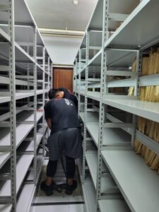 師傅站在密集白色鐵製書架之間組裝固定層板，代客搬家完成機關檔案室鐵架安裝