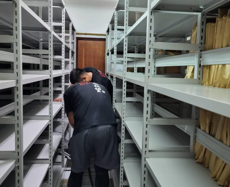 師傅站在密集白色鐵製書架之間組裝固定層板，代客搬家完成機關檔案室鐵架安裝