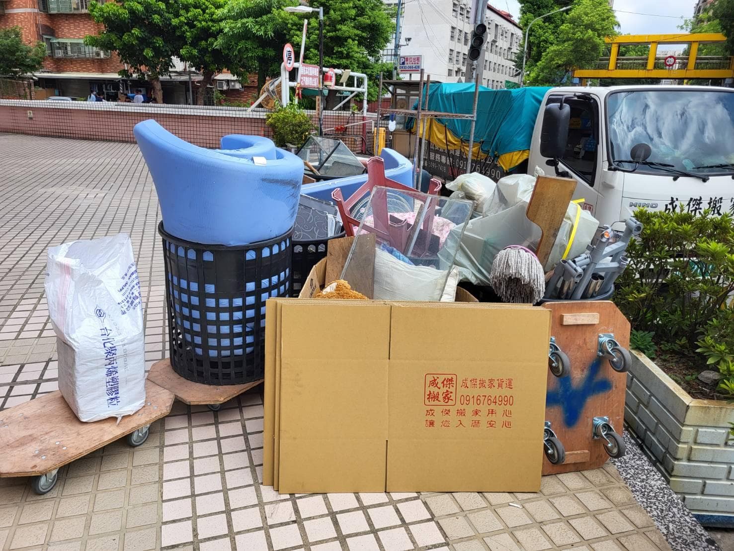 成傑搬家紙箱與雜物堆放在推車上,後方停有品牌貨車,搬家作業現場實況