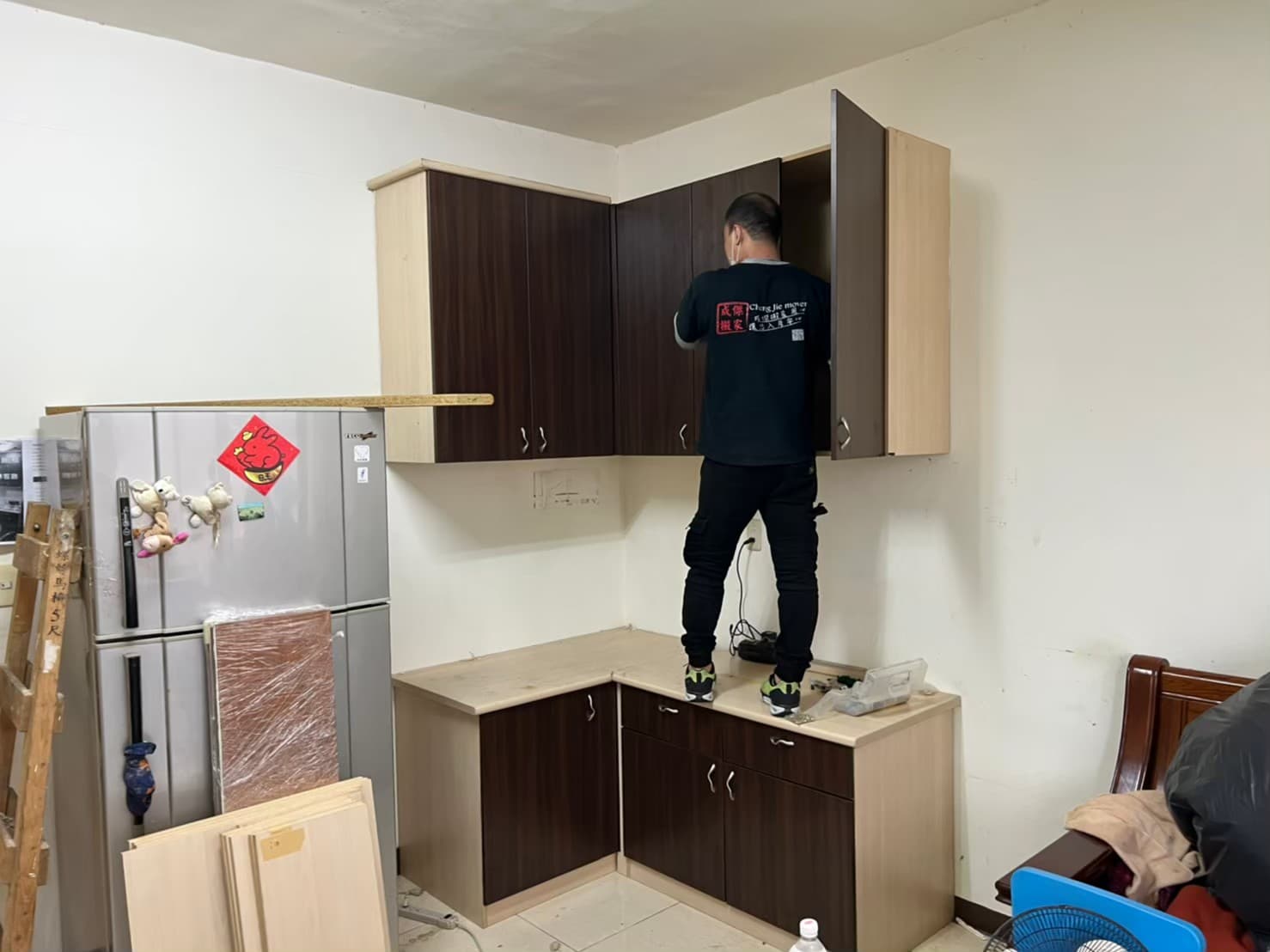 成傑搬家工作人員站在廚房安裝深色木紋系統吊櫃,代客搬家同步協助廚具定位