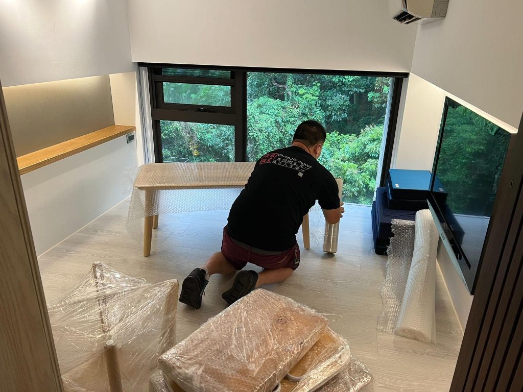 成傑搬家工作人員在客廳用保護膜包裝原木色長形餐桌桌腳，家庭搬家打包作業