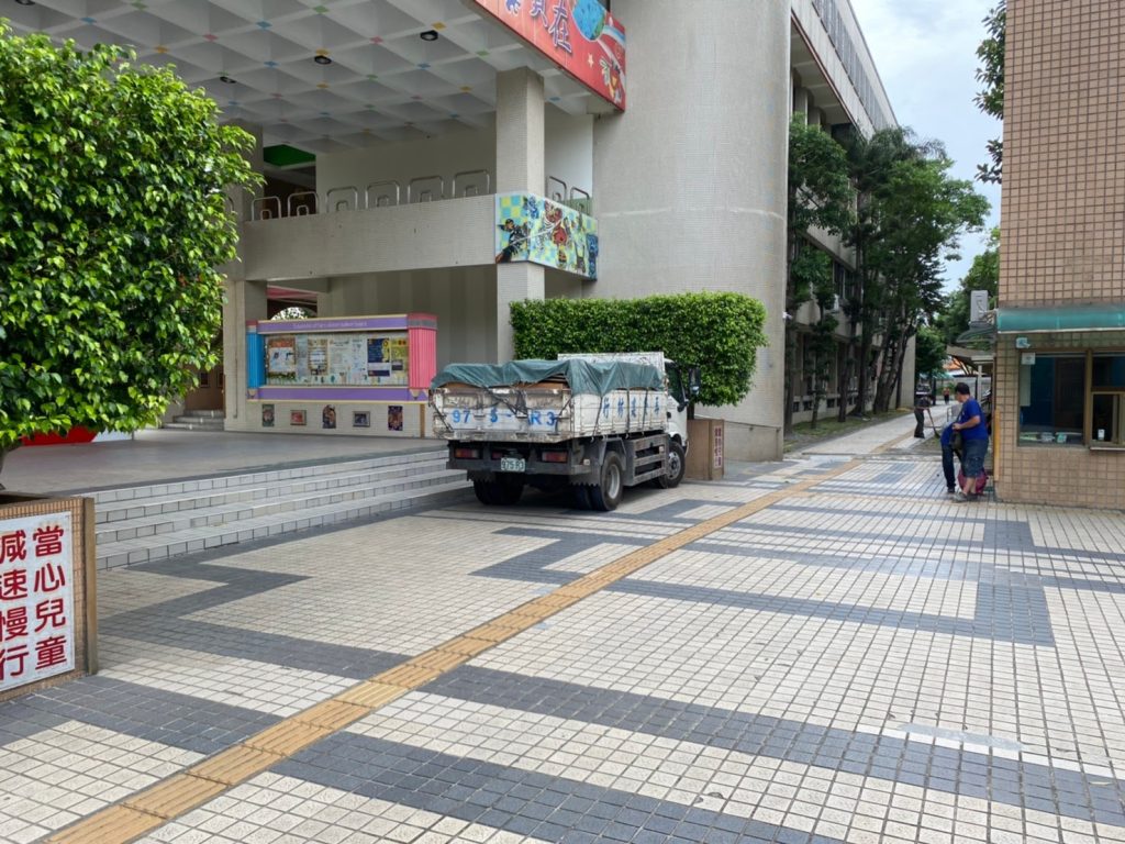 成傑搬家小型貨車以藍色帆布覆蓋貨物，停靠建築入口廣場，準備執行搬運作業