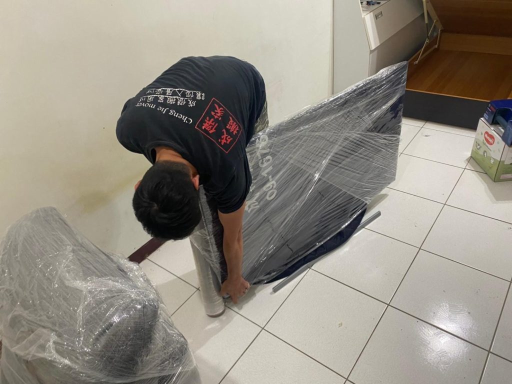 成傑搬家師傅穿著制服以保鮮膜纏繞固定深藍色彈簧床墊，家庭搬家確實打包