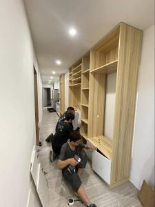 成傑搬家兩名工作人員跪地合力組裝高大原木色系統書牆，代客搬家入住後組裝服務